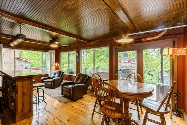 2232 Birchwood Dr NE, Cedar Rapids, IA 52402 - dining space with light wood-style flooring, wooden ceiling with exposed beams, a ceiling fan, a fireplace, and wood walls