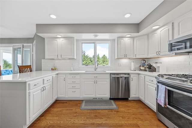 1355 Red Star Rd, Tipton, IA 52772 - kitchen with appliances with stainless steel finishes, a sink, a peninsula, light wood-type flooring, and backsplash