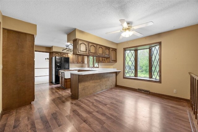 4633 Northwood Dr NE, Cedar Rapids, IA 52402 - kitchen with black fridge, a peninsula, dark wood-style flooring, a textured ceiling, and a ceiling fan