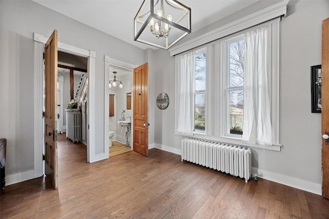 320 E St, Tipton, IA 52772 - empty room featuring radiator heating unit, a chandelier, baseboards, and wood finished floors