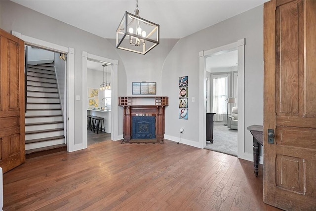 320 E St, Tipton, IA 52772 - living area with a chandelier, wood-type flooring, a fireplace with flush hearth, stairs, and baseboards