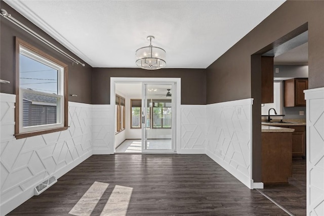 3013 Ravenwood Ter NW, Cedar Rapids, IA 52405 - unfurnished dining area with a chandelier, wainscoting, dark wood-style flooring, a ceiling fan, and a sink