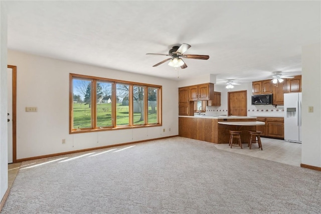 6405 Hillcrest Rd, Cedar Rapids, IA 52404 - kitchen with white fridge with ice dispenser, black microwave, ceiling fan, and brown cabinets