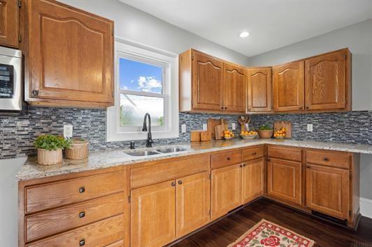 611 3rd Ave NE, Independence, IA 50644 - kitchen featuring a sink, stainless steel microwave, dark wood-type flooring, decorative backsplash, and brown cabinets