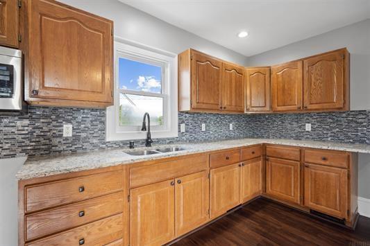 611 3rd Ave NE, Independence, IA 50644 - kitchen featuring a sink, stainless steel microwave, dark wood-style floors, decorative backsplash, and brown cabinets
