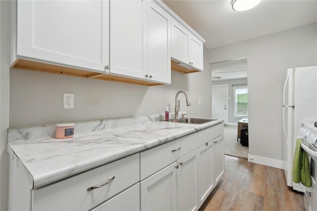 944 L St SW, Cedar Rapids, IA 52404 - kitchen with a sink, light wood-type flooring, white cabinets, white stove, and baseboards