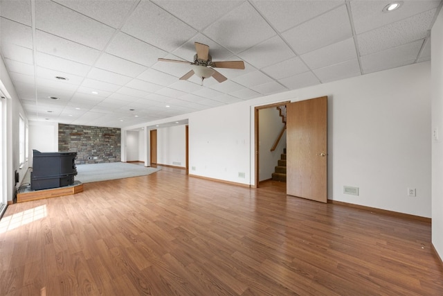 3017 Peaceful Dr, Riverside, IA 52327 - unfurnished living room with a wood stove, ceiling fan, wood finished floors, stairs, and a paneled ceiling