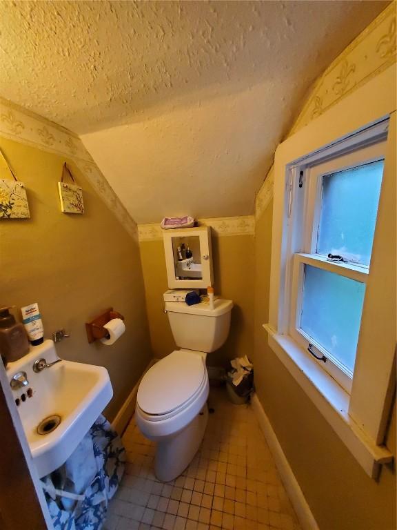 1114 2nd Ave, Vinton, IA 52349 - bathroom with lofted ceiling, a textured ceiling, toilet, tile patterned flooring, and a sink