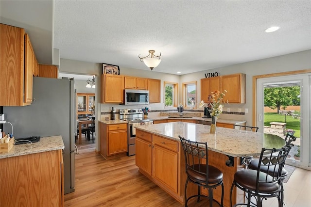 7025 Walden Rd NE, Cedar Rapids, IA 52402 - kitchen featuring stainless steel appliances, a kitchen breakfast bar, a kitchen island, light wood-type flooring, and light stone countertops