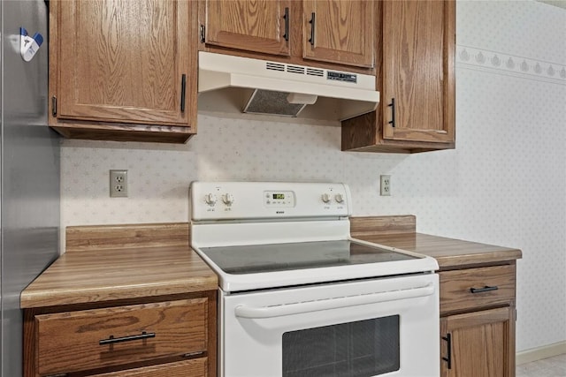 4111 Blue Jay Dr NE Unit A, Cedar Rapids, IA 52402 - kitchen with white range with electric cooktop, under cabinet range hood, wallpapered walls, freestanding refrigerator, and brown cabinetry