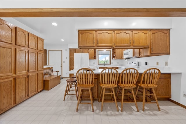 1782 Baker Ave, West Branch, IA 52358 - kitchen featuring a peninsula, white appliances, brown cabinets, a kitchen bar, and light countertops