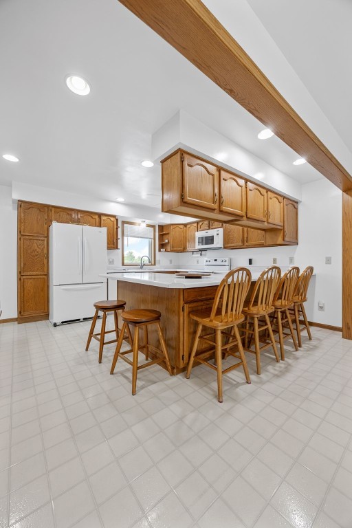 1782 Baker Ave, West Branch, IA 52358 - kitchen with white appliances, light countertops, a kitchen bar, brown cabinets, and recessed lighting