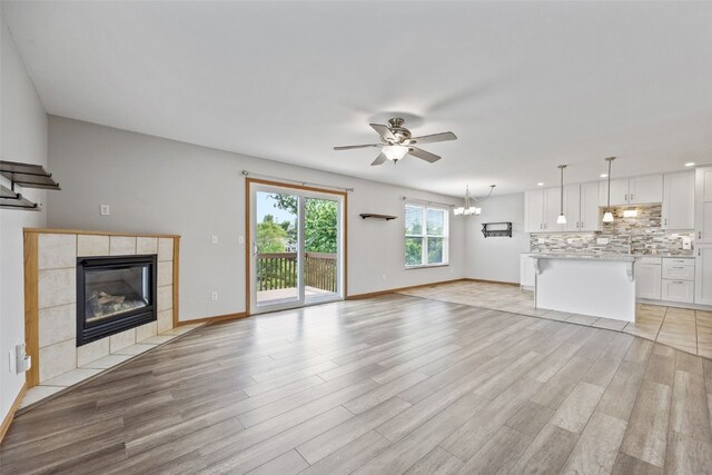 2273 Holiday Rd, Coralville, IA 52241 - unfurnished living room with a ceiling fan, a tiled fireplace, light wood-style flooring, baseboards, and a chandelier