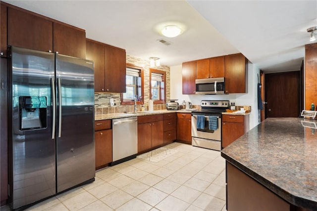 331 Lake View Dr NE, Solon, IA 52333 - kitchen featuring stainless steel appliances, a sink, light tile patterned flooring, dark countertops, and backsplash