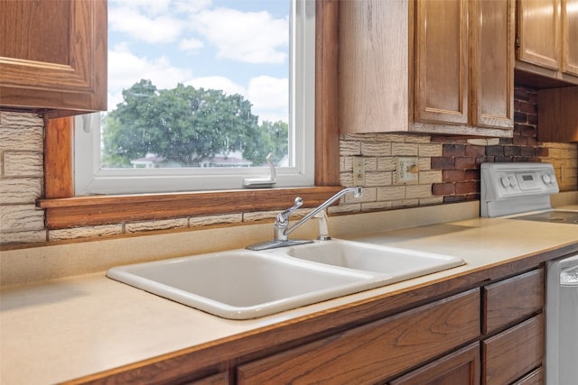 502 5th Ave, Clarence, IA 52216 - kitchen featuring a sink, backsplash, brown cabinetry, stainless steel dishwasher, and light countertops
