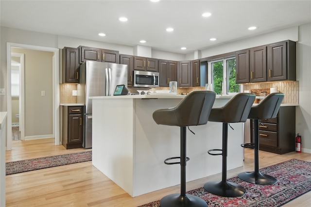 1649 Memorial Dr SE, Cedar Rapids, IA 52403 - kitchen with appliances with stainless steel finishes, light wood-style floors, a breakfast bar area, backsplash, and recessed lighting