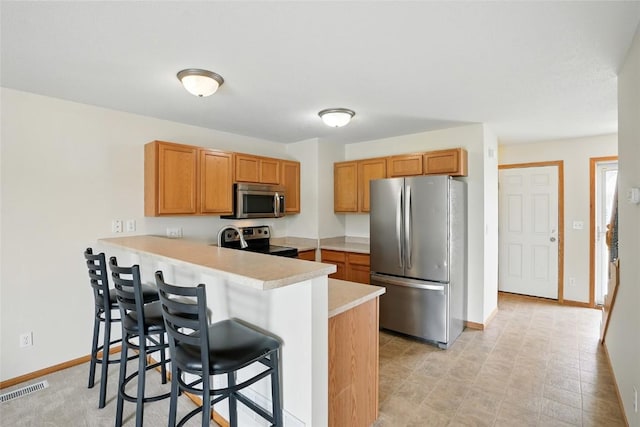 1450 Tower Ln NE, Cedar Rapids, IA 52402 - kitchen with stainless steel appliances, light countertops, a peninsula, a kitchen breakfast bar, and baseboards