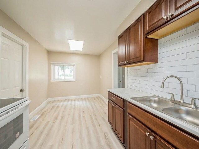 207 Prospect St NW, Blairstown, IA 52209 - kitchen with a skylight, tasteful backsplash, light wood-style flooring, light countertops, and white range with electric stovetop