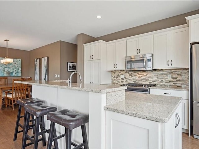 100 4th Ave SW Unit 204, Cedar Rapids, IA 52404 - kitchen with appliances with stainless steel finishes, a kitchen island with sink, backsplash, white cabinets, and wood finished floors