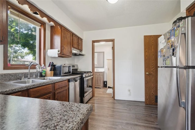 1802 9th Ave, Belle Plaine, IA 52208 - kitchen with appliances with stainless steel finishes, under cabinet range hood, wood finished floors, and brown cabinets