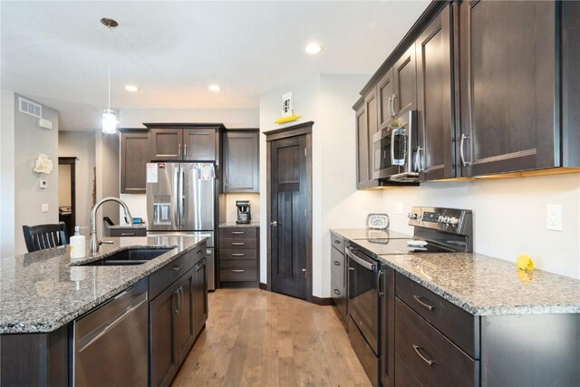 1602 Bridge Creek Ct, Marion, IA 52302 - kitchen featuring appliances with stainless steel finishes, dark brown cabinets, light wood-style floors, light stone counters, and hanging light fixtures