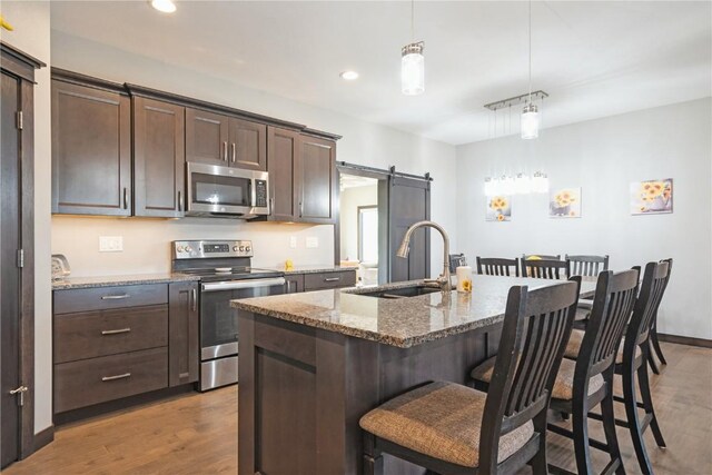 1602 Bridge Creek Ct, Marion, IA 52302 - kitchen with stainless steel appliances, a barn door, dark brown cabinetry, light wood-style floors, and light stone countertops