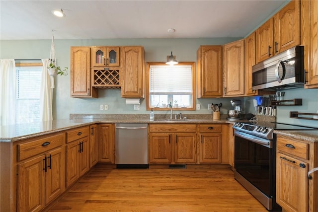 765 34th Ave, Marion, IA 52302 - kitchen featuring appliances with stainless steel finishes, light wood finished floors, light stone counters, a peninsula, and brown cabinetry
