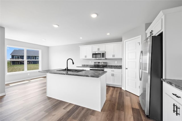 5007 Dostal Dr, Cedar Rapids, IA 52404 - kitchen featuring appliances with stainless steel finishes, dark wood-style flooring, white cabinets, a kitchen island with sink, and dark stone countertops
