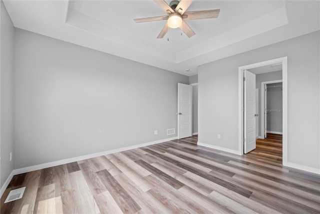 5007 Dostal Dr, Cedar Rapids, IA 52404 - unfurnished bedroom featuring a tray ceiling, wood finished floors, a walk in closet, and ceiling fan
