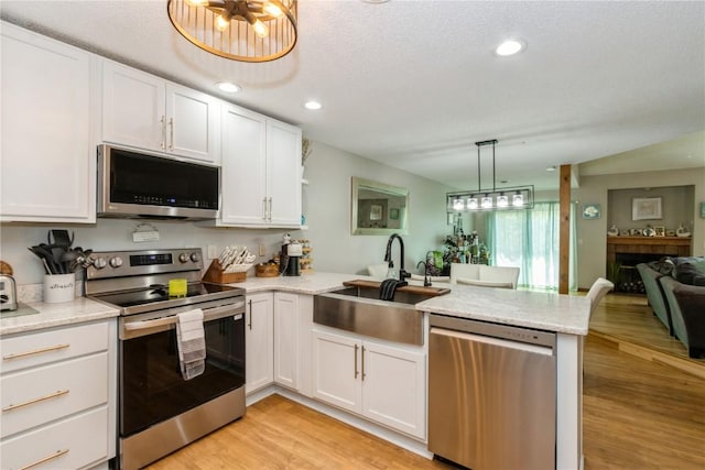 1932 N Ridge Dr, Coralville, IA 52241 - kitchen with stainless steel appliances, a peninsula, white cabinetry, light wood finished floors, and open floor plan