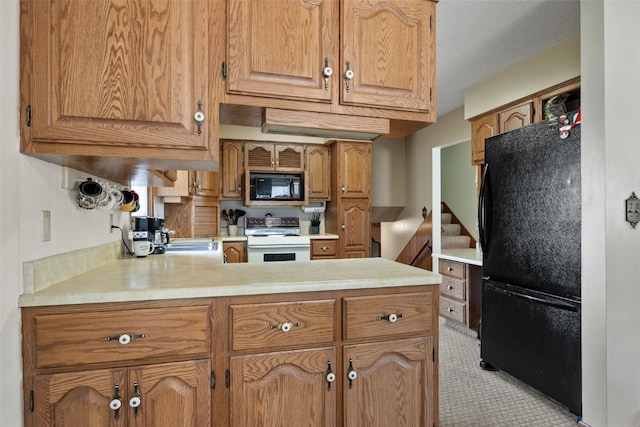 105 Parkview Dr, Tipton, IA 52772 - kitchen with black appliances, a peninsula, light countertops, brown cabinetry, and light colored carpet