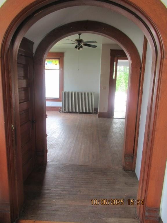 606 Meridian St, Tipton, IA 52772 - corridor featuring radiator heating unit, arched walkways, and hardwood / wood-style flooring
