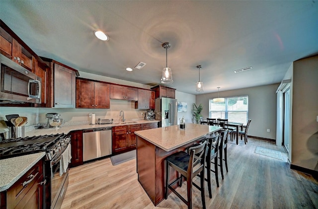 1004 Creekside Dr, Tiffin, IA 52340 - kitchen featuring stainless steel appliances, a kitchen bar, light wood-style flooring, decorative light fixtures, and a kitchen island