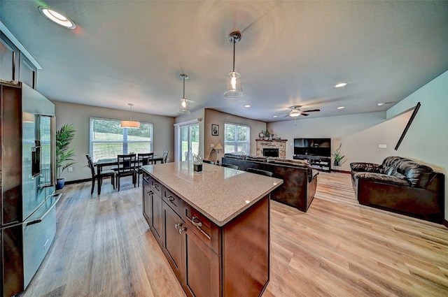 1004 Creekside Dr, Tiffin, IA 52340 - kitchen featuring a fireplace, light wood-type flooring, a ceiling fan, a kitchen island, and light stone counters