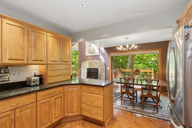2520 NE Sugar Bottom Rd, Solon, IA 52333 - kitchen featuring freestanding refrigerator, light wood-style floors, a chandelier, dark stone counters, and a high end fireplace