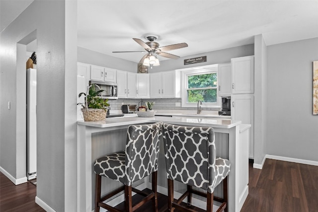 1428 Timber Ridge Trl NE, Solon, IA 52333 - kitchen with stainless steel microwave, white cabinets, a kitchen bar, decorative backsplash, and light countertops