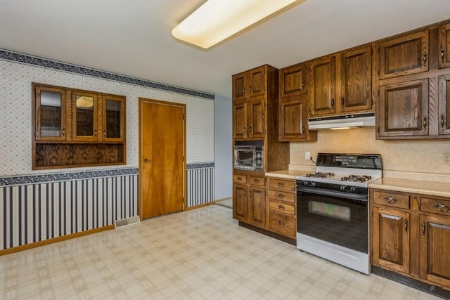 5660 Briarwood St SW, Cedar Rapids, IA 52401 - kitchen with gas range gas stove, under cabinet range hood, wallpapered walls, light countertops, and glass insert cabinets