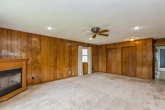 5660 Briarwood St SW, Cedar Rapids, IA 52401 - unfurnished living room featuring ceiling fan, carpet, a glass covered fireplace, wooden walls, and recessed lighting