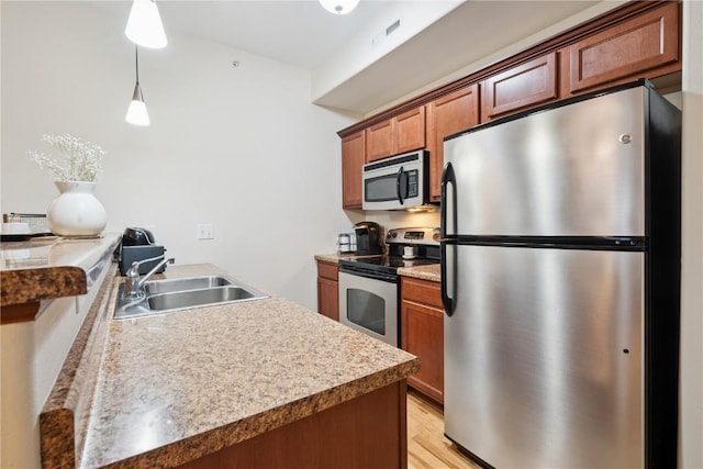 1848 W Benton St, Iowa City, IA 52246 - kitchen featuring appliances with stainless steel finishes, light wood-style flooring, brown cabinets, pendant lighting, and a peninsula