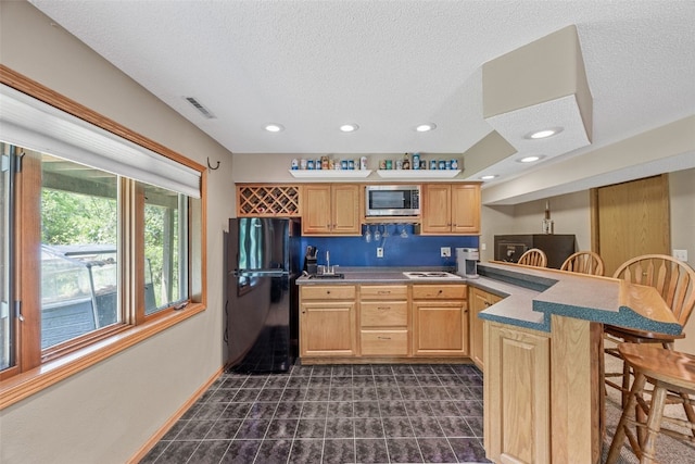 3496 E Otter Rd, Marion, IA 52302 - kitchen with stainless steel microwave, freestanding refrigerator, a breakfast bar area, light brown cabinetry, and a textured ceiling