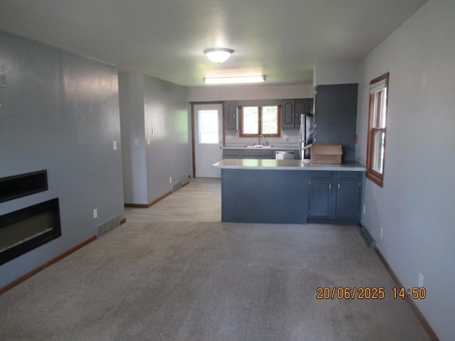 302 Meridian St, Tipton, IA 52772 - kitchen featuring a peninsula, light countertops, light colored carpet, freestanding refrigerator, and dishwashing machine