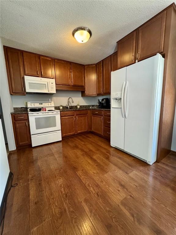 72 Fleetwood Rd NW, Cedar Rapids, IA 52405 - kitchen with white appliances, dark wood-type flooring, dark countertops, a textured ceiling, and brown cabinetry