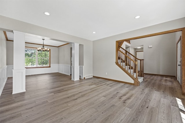 7603 Hampshire Dr NE, Cedar Rapids, IA 52402 - unfurnished living room with decorative columns, a chandelier, stairway, a wainscoted wall, and wood finished floors