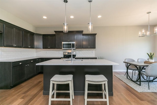 806 Crestview Dr, Solon, IA 52333 - kitchen with appliances with stainless steel finishes, a chandelier, wood finished floors, decorative backsplash, and recessed lighting