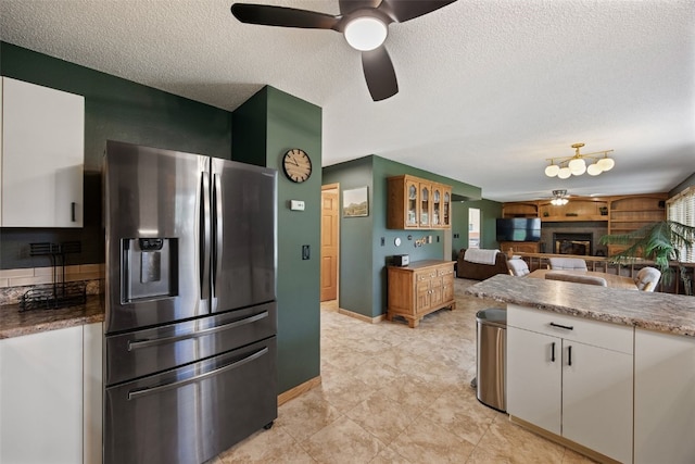 1720 Charleston Dr, Marion, IA 52302 - kitchen featuring stainless steel fridge with ice dispenser, a glass covered fireplace, a textured ceiling, white cabinets, and a ceiling fan