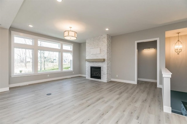 5750 Meadow Grass Cir SE, Cedar Rapids, IA 52403 - unfurnished living room with light wood-style flooring, recessed lighting, a stone fireplace, and a chandelier