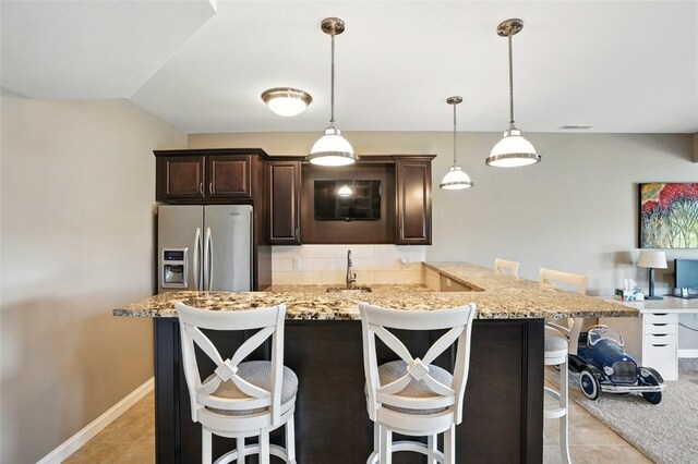 701 Sherwood Dr, Iowa City, IA 52245 - kitchen with stainless steel fridge, dark brown cabinets, a breakfast bar area, and light tile patterned floors