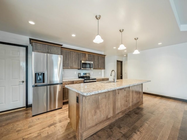 3502 Bluebird Dr SW, Cedar Rapids, IA 52404 - kitchen with stainless steel appliances, light wood-style floors, an island with sink, dark brown cabinetry, and backsplash