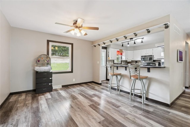 1708 Woodside Ct NW, Cedar Rapids, IA 52405 - kitchen featuring stainless steel microwave, white cabinetry, ceiling fan, wood finished floors, and a kitchen bar