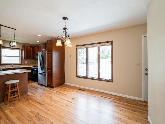 4634 Twin Pine Dr NE, Cedar Rapids, IA 52402 - kitchen featuring freestanding refrigerator, black gas stove, light wood finished floors, light countertops, and a kitchen breakfast bar